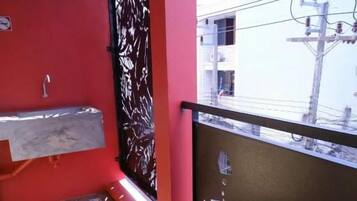 A balcony with a red wall, a black metal gate, and a view of buildings in the background.