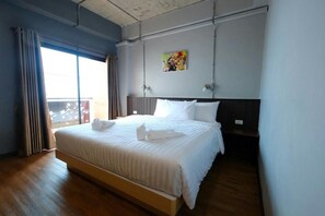 A hotel room with a large bed, a painting on the wall, and a view through the window. - Room2u (Hat Yai)