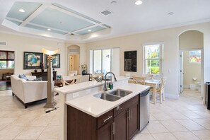 A spacious kitchen with a central island, a dining area with a table and chairs, and a living room with a sofa and a coffee table. - Serene University Park Golf & Country Club Pool Home - Gulf Standard (Bradenton)