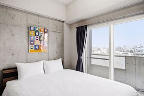 Habitación de hotel con una cama grande, una pared de concreto y vistas a la ciudad a través de una ventana.