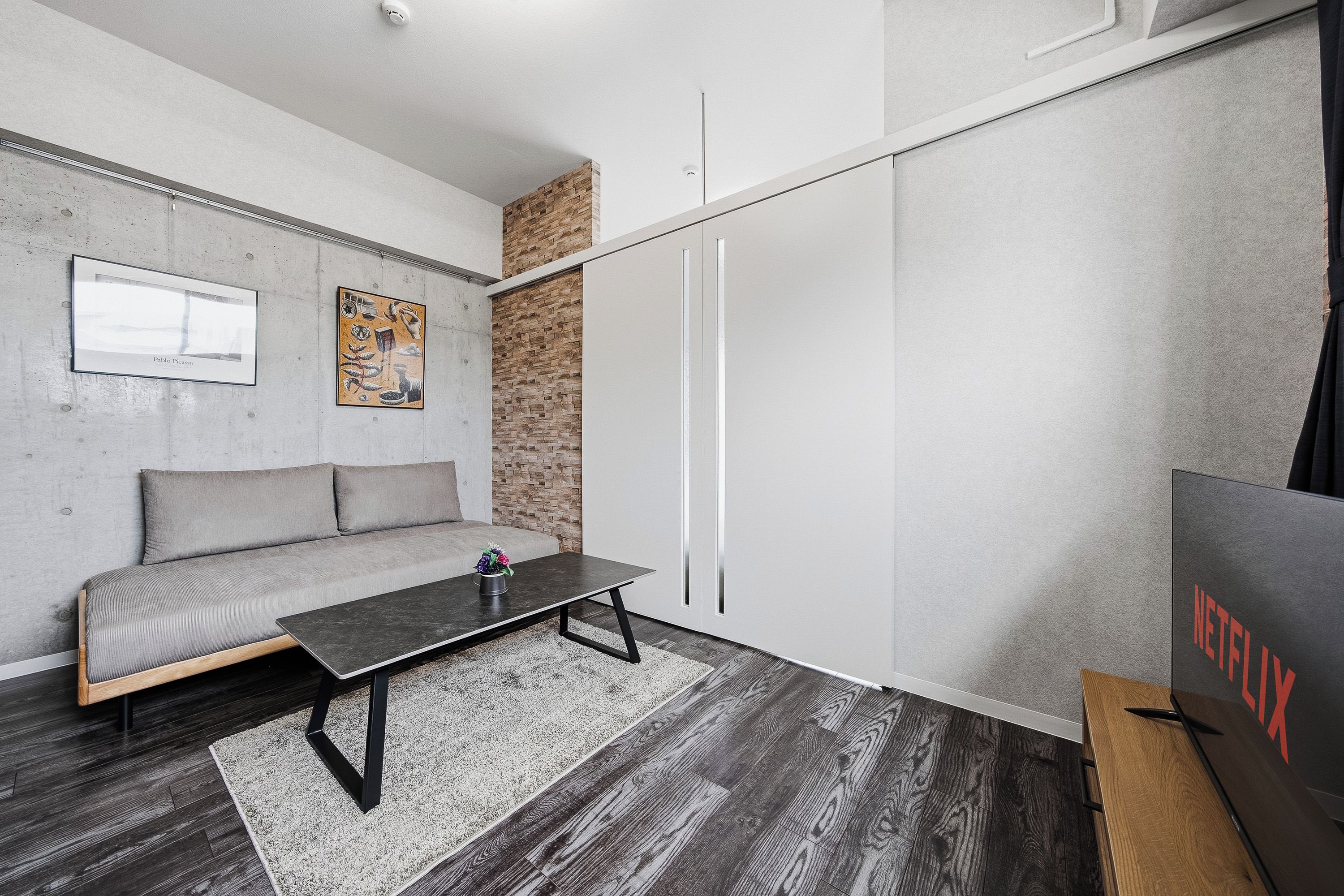 A modern living room with a grey sofa, a coffee table, and a wall-mounted artwork.