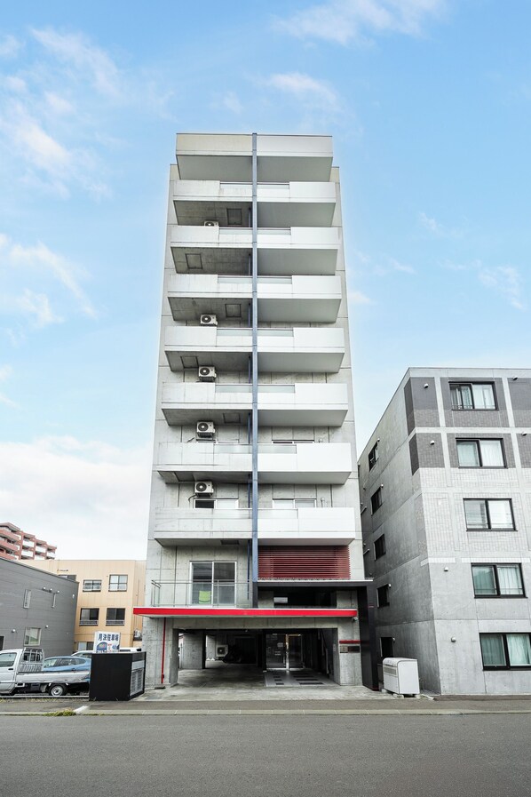 Un edificio de varios pisos con un hueco central para ascensor, balcones en cada planta y unidades de aire acondicionado.