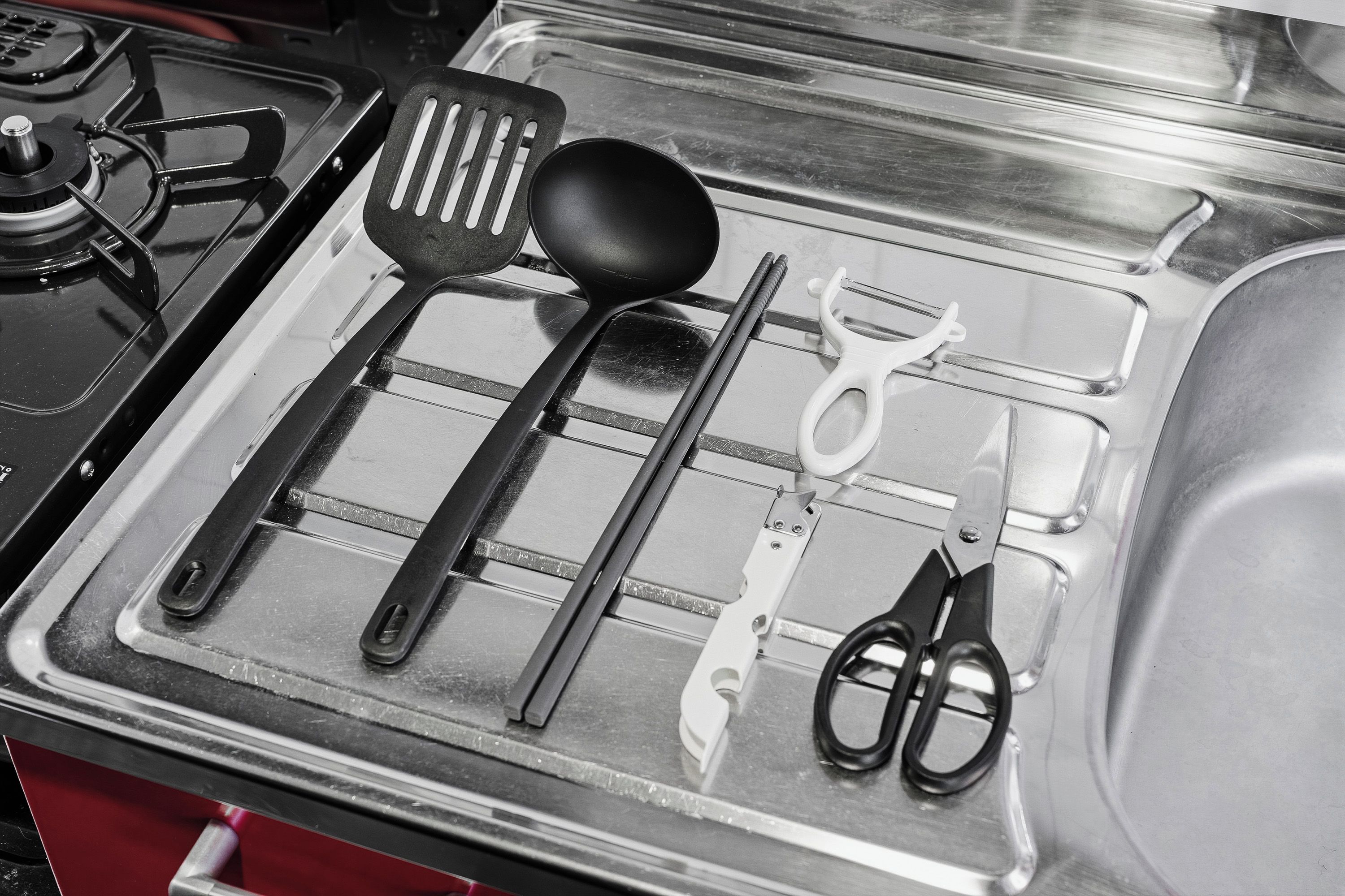A stainless steel kitchen sink with various utensils like a spatula, ladle, and scissors.