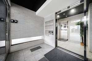 Una entrada moderna de edificio con puerta de vidrio, planta en maceta y suelo de baldosas.