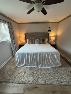 A bedroom with a bed, a ceiling fan, two bedside lamps, a window with blinds, and a carpeted floor. - Oxford Condo ~ Walk to Campus (Oxford)