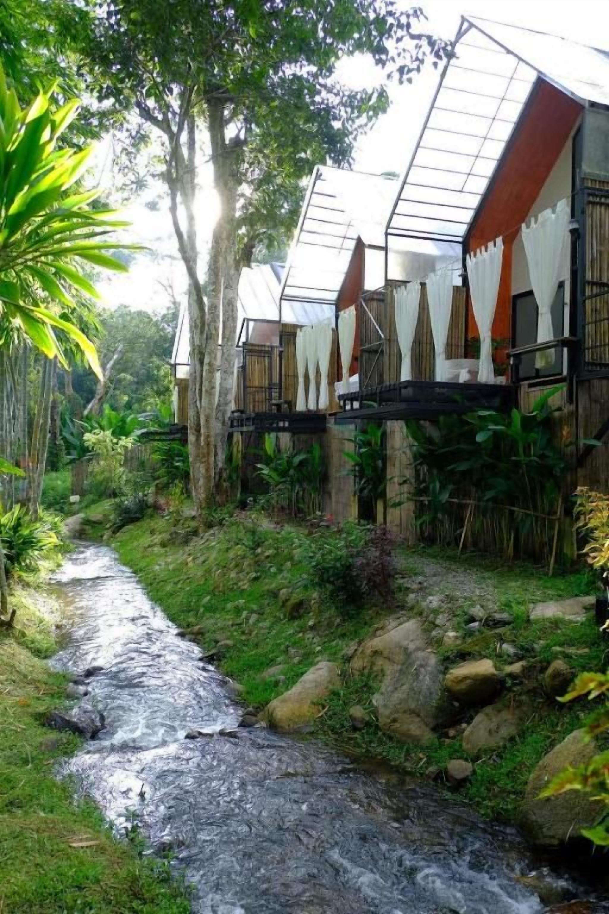 Un entorno natural con un arroyo, árboles y una serie de edificios de estilo arquitectónico moderno.