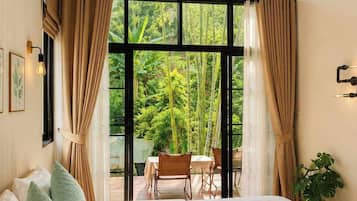 Un dormitorio con una cama grande, una ventana con cortinas, una mesa con sillas afuera y una planta.