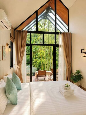 A bedroom with a large bed, a window with curtains, a table with chairs outside, and a plant. - Chertarn Homestay (Doisaket)
