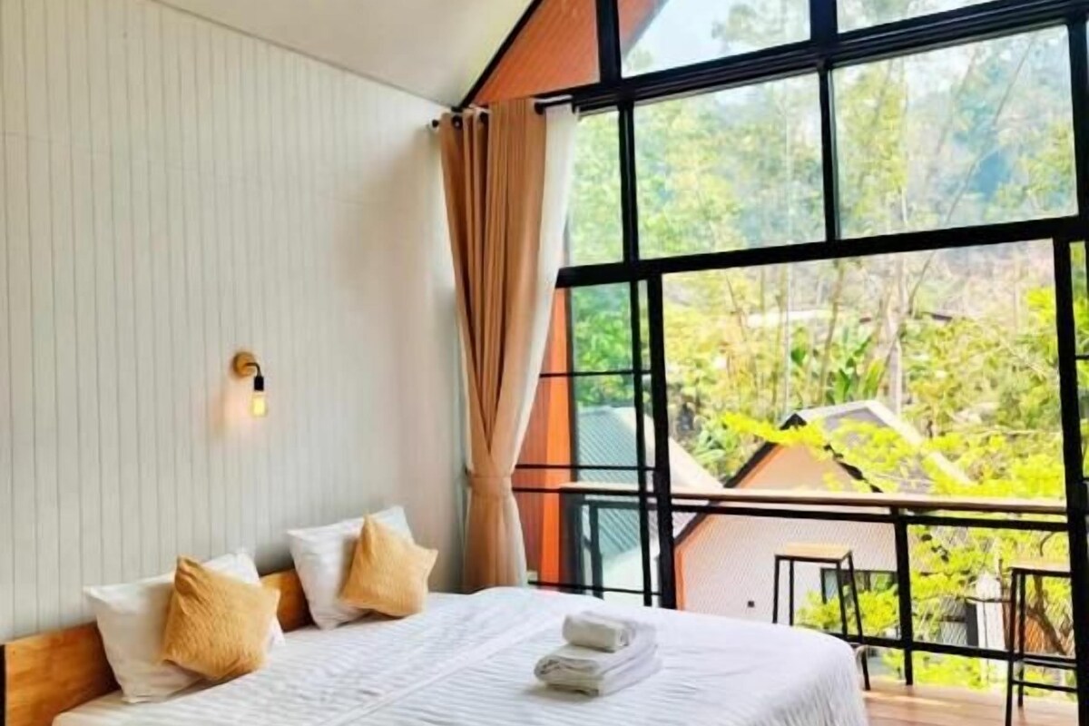 A modern bedroom with a large window, a wooden bed, and a view of greenery outside.