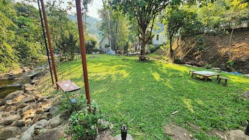Un espacio al aire libre con césped, un pequeño arroyo, mesas de picnic y una hamaca.