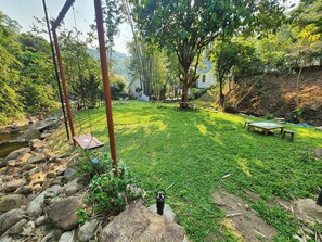 A grassy outdoor area with a small stream, picnic tables, and a hammock. - Chertarn Homestay (Doisaket)