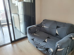 A modern living room with a sofa, a glass door leading to a balcony, and a kitchen area visible through the glass. - 10 minutes walk to BTS bangna BITEC resort style condo 3 swimming pools 2 gyms (Krung Thep Maha Nakhon)