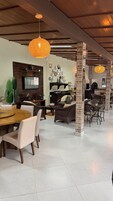 Uma sala espaçosa com mesa de jantar, móveis de vime e uma cozinha equipada, incluindo televisão e pratos decorativos.