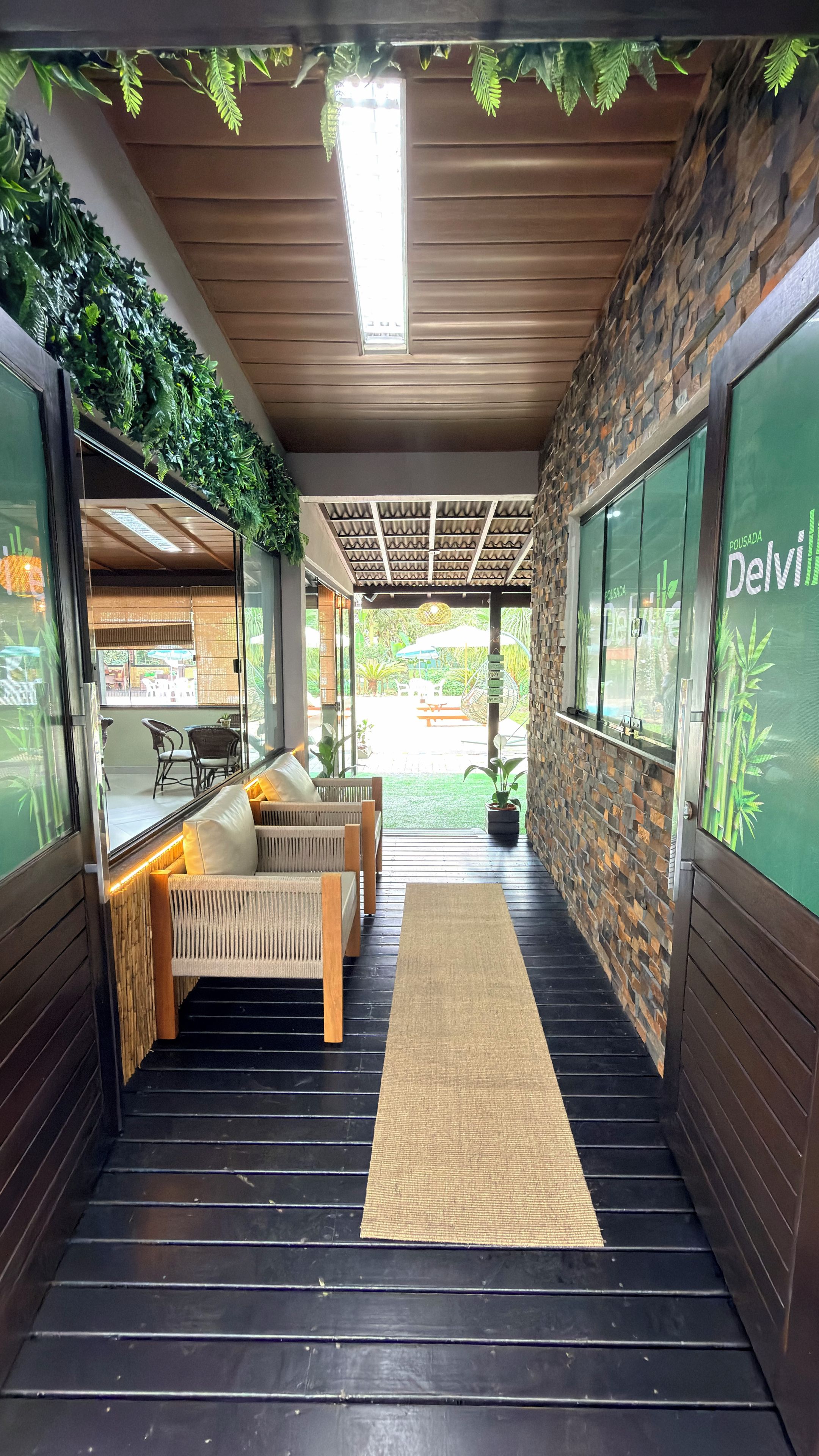 A corridor with a wooden ceiling, a woven bench, and a rug leading to an outdoor area with a table and chairs.