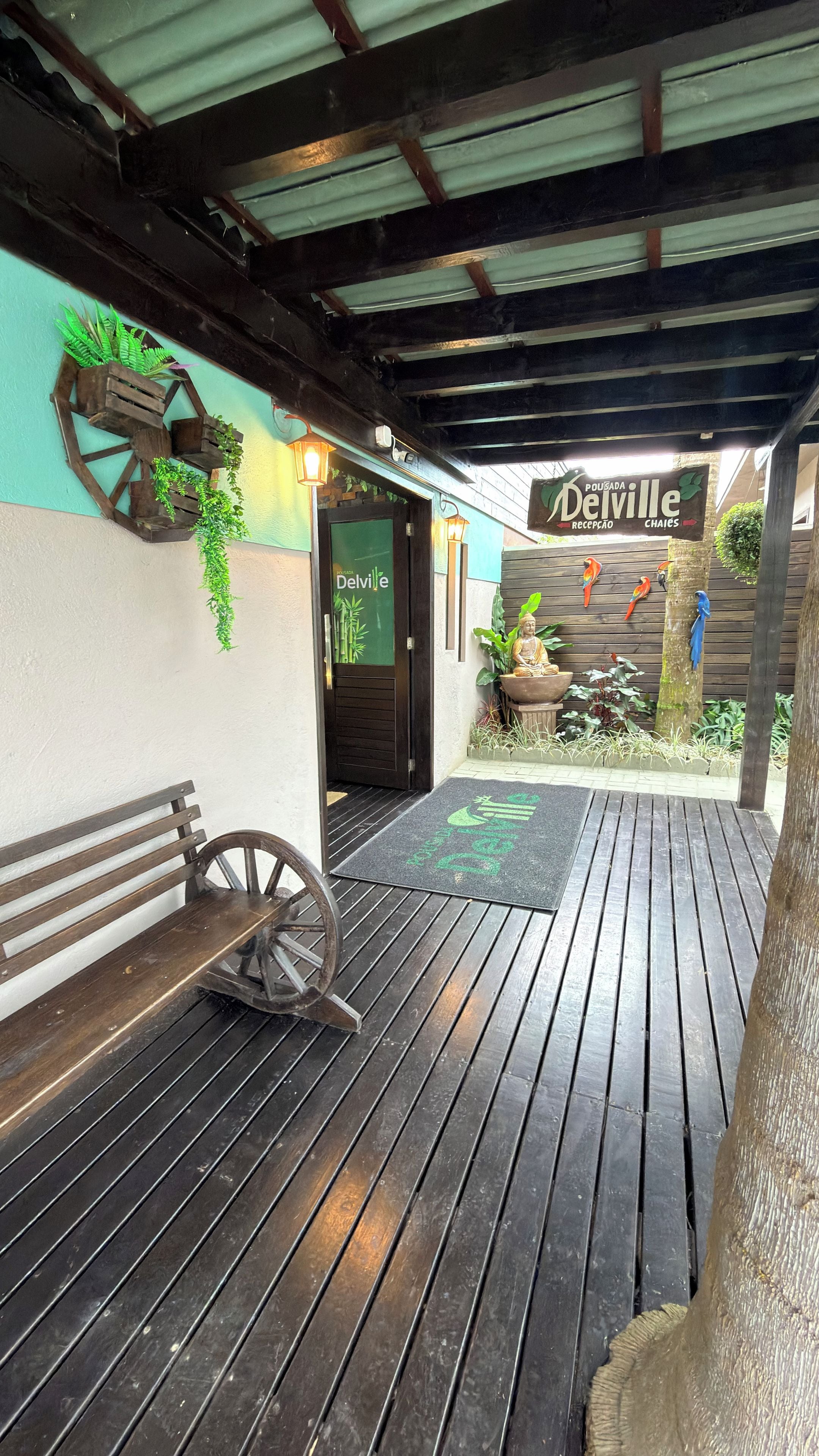 Une terrasse en bois avec un banc, un mur rustique agrémenté de plantes et une enseigne indiquant « Pousada Delville ».