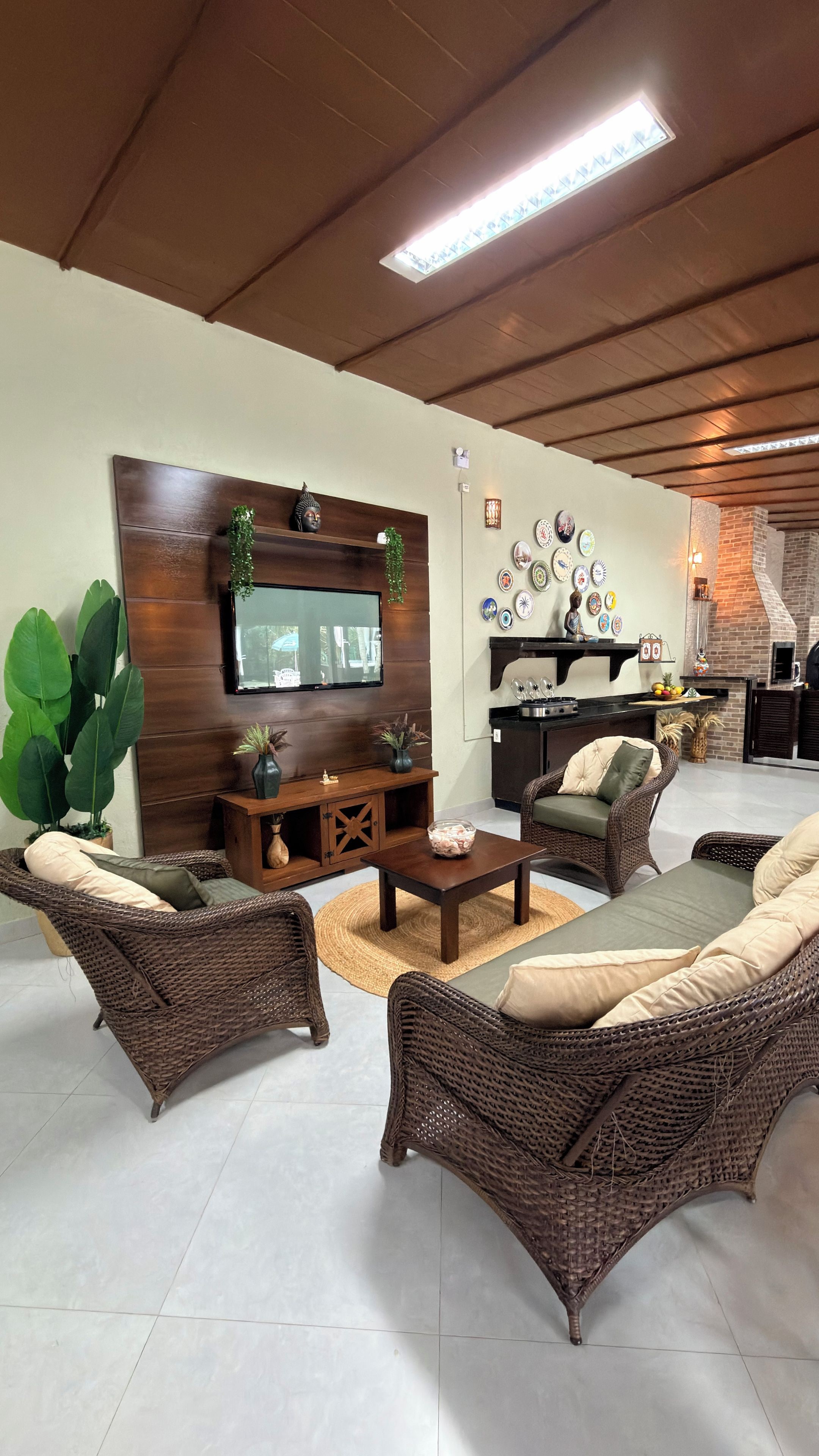 A living room with wicker furniture, a flat-screen TV, and a kitchen area with a brick oven.