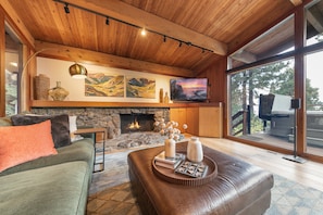 A cozy living room with a stone fireplace, a leather sofa, and a flat-screen TV mounted on the wall. - Topaz Lake View at Dollar Point by Tahoe Getaways - Pet-Friendly 5BR w/ Private Hot Tub (Tahoe City)