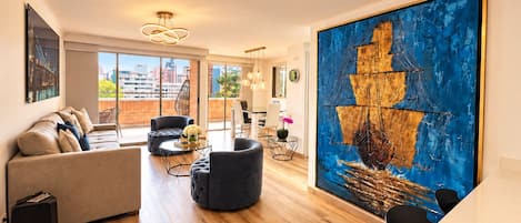 A spacious living room with a large abstract painting, a sofa, a coffee table, and a dining area with chairs.