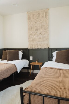 Ein Zimmer mit zwei Betten, jeweils mit einer braunen Decke, einem kleinen Holz-Nachttisch und einer Wanddekoration.