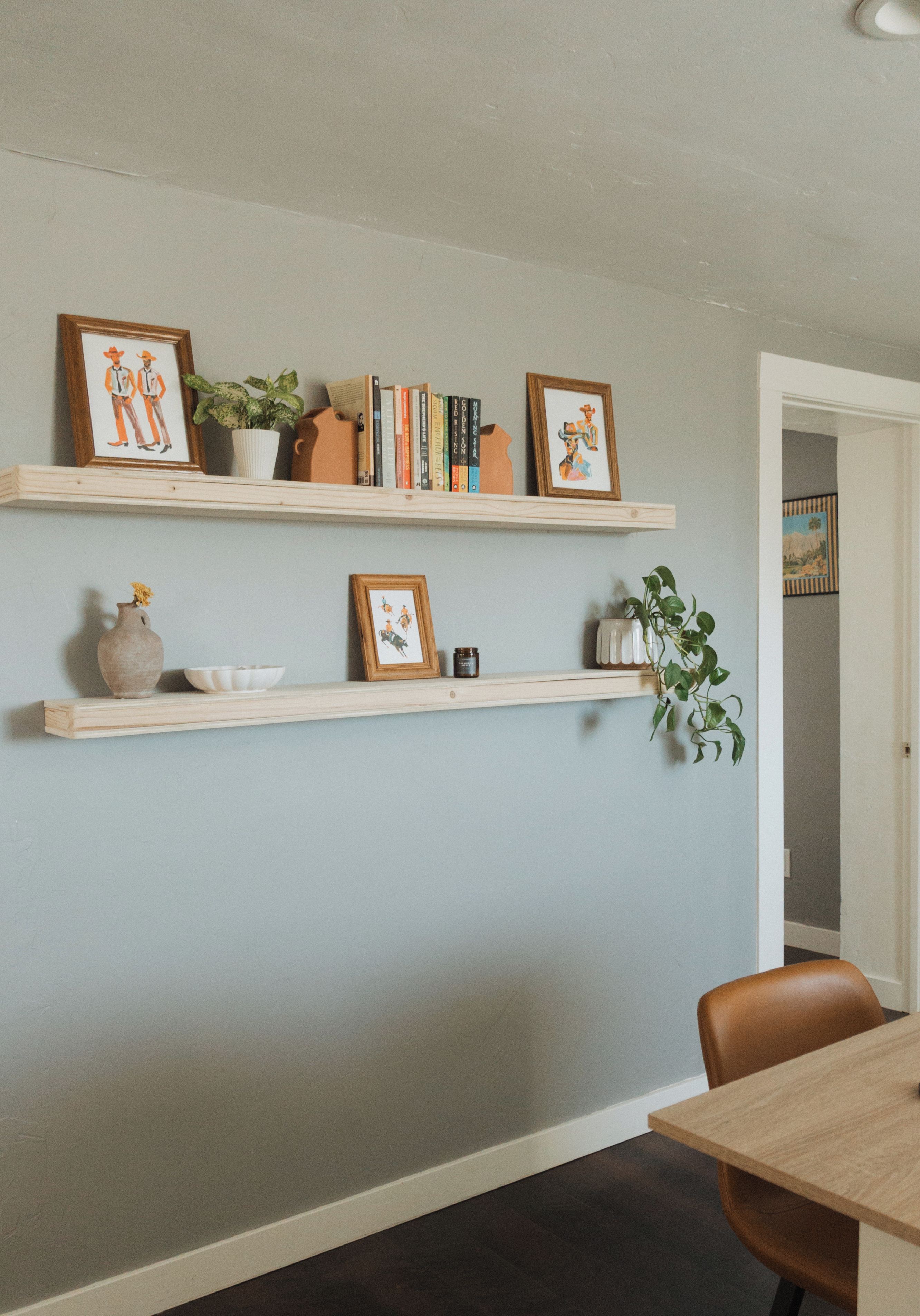 A room with two wooden shelves against a wall, each holding various items including framed pictures, books, and decorative objects.