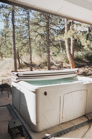 Ein Whirlpool in einem überdachten Außenbereich mit Bäumen im Hintergrund.