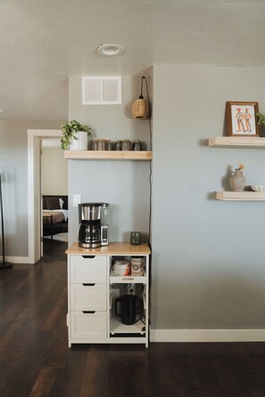 Une petite cuisine équipée d’une machine à café, de placards de rangement et d’une petite étagère avec des bocaux.