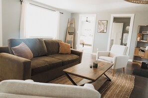 Ein Wohnzimmer mit einem braunen Sofa, einem weißen Sessel, einem Couchtisch und einem Bücherregal.