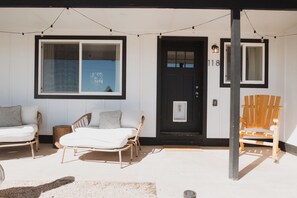 A porch with two wicker chairs and a wooden chair, a black door, and a window with a view. - Enjoyable 3-bedroom house in Palmer Lake perfect for your getaway (Palmer Lake)