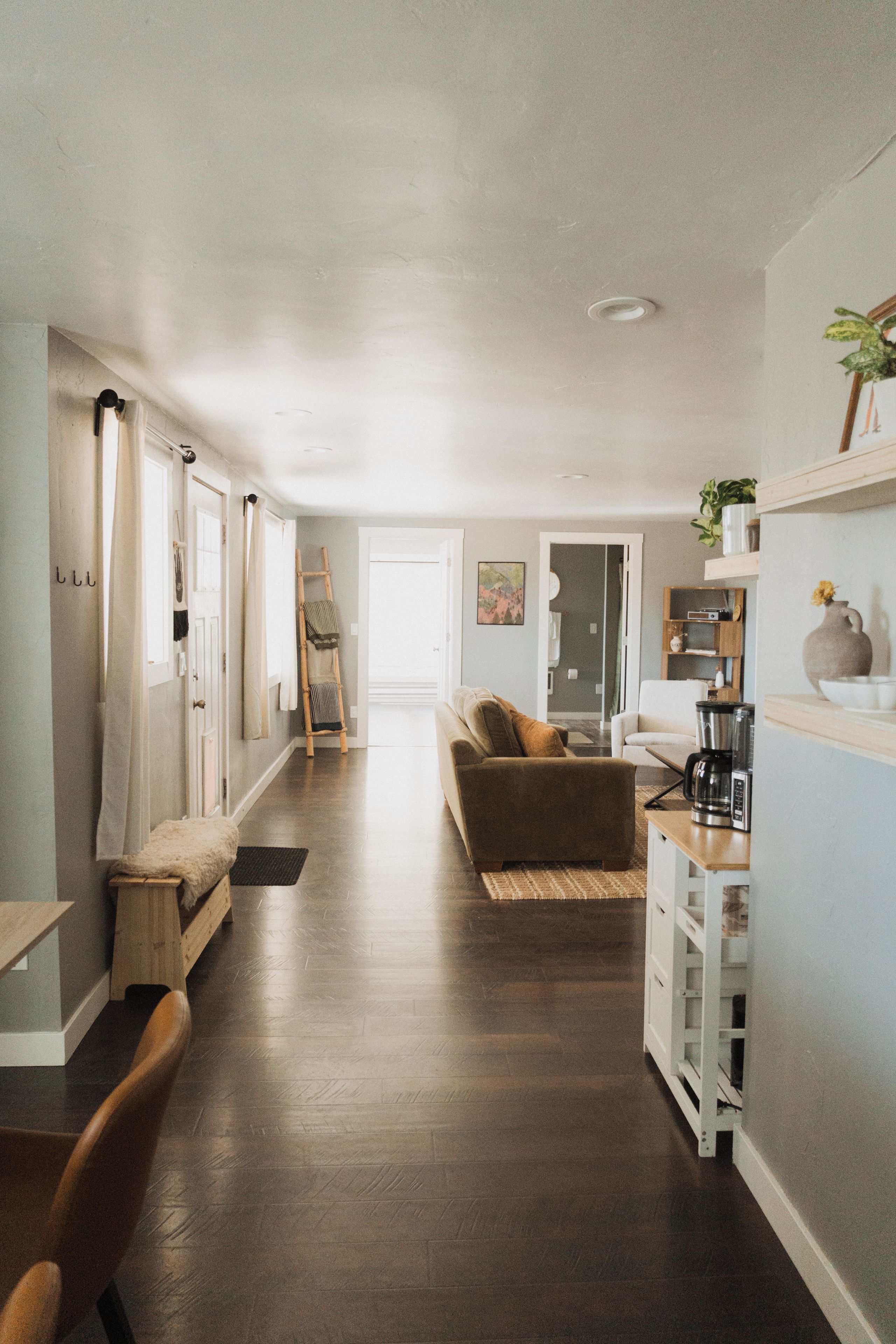 A hallway leading to a living area with a sofa and coffee table, wooden flooring, and a staircase.