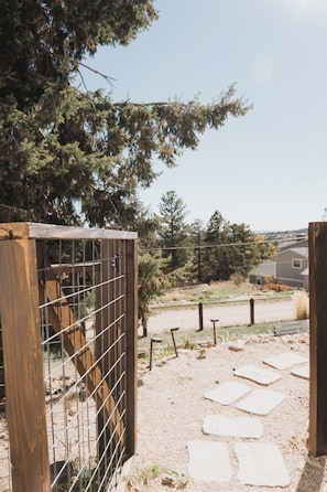 A wooden gate with metal bars, a stone pathway, and a view of a residential area with houses and trees. - Enjoyable 3-bedroom house in Palmer Lake perfect for your getaway (Palmer Lake)