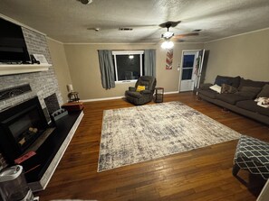 Ein Wohnzimmer mit Kamin, einer Couch, einem Sessel und einem gemusterten Teppich.