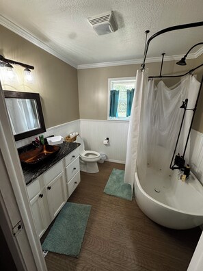 Ein Badezimmer mit einer Badewanne, Toilette, Waschbecken und einem Fenster mit Vorhängen.