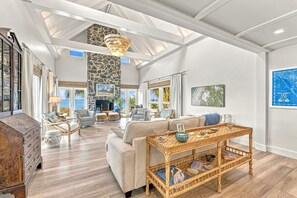 A spacious living room with a high ceiling, a stone accent wall, and a large window overlooking a scenic view. - White Heron | Beachfront Gulf Views, Access to Pool, Manasota Key (Englewood)