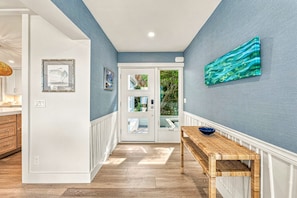 A hallway with a wooden bench, a door with glass panels, and a wall-mounted painting. - White Heron | Beachfront Gulf Views, Access to Pool, Manasota Key (Englewood)