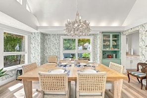A dining room with a large wooden table, wicker chairs, and a chandelier. - White Heron | Beachfront Gulf Views, Access to Pool, Manasota Key (Englewood)