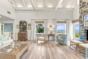 A spacious living room with a view of the ocean, wooden flooring, and a stone fireplace. - White Heron | Beachfront Gulf Views, Access to Pool, Manasota Key (Englewood)