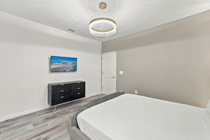 A bedroom with a bed, a TV mounted on the wall, a dresser, and a door. - Sonoma Resort | 15BR Mansion, Pool, Sleeps 30 (Kissimmee)