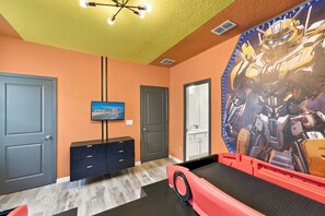 A room with a large robot-themed mural, a television, a cabinet, and a door. - Sonoma Resort | 15BR Mansion, Pool, Sleeps 30 (Kissimmee)
