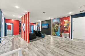 Un interior moderno con suelo de madera, paredes rojas y azules, y obras de arte que incluyen un superhéroe.