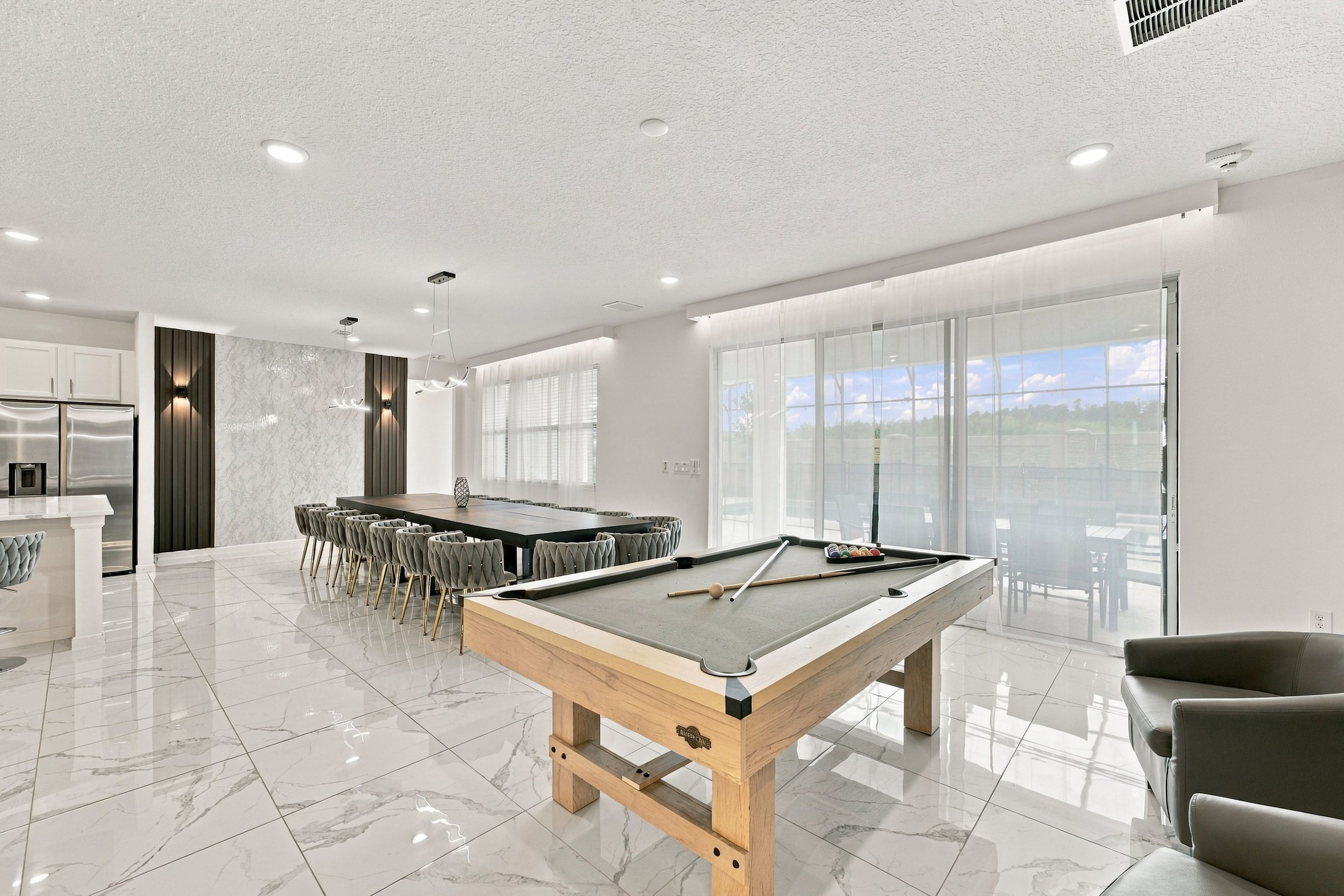 Une table de billard moderne pour l’intérieur, avec une queue de billard, un coin repas avec des chaises et une cuisine équipée d’un réfrigérateur.