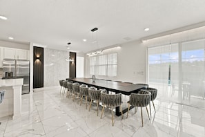 A modern kitchen with a large island, stainless steel appliances, and a dining area with a long table and chairs. - Sonoma Resort | 15BR Mansion, Pool, Sleeps 30 (Kissimmee)