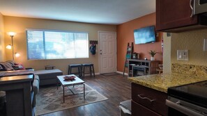 Un espacio habitable compacto con kitchenette, zona de comedor y de estar con sofá y sillas.
