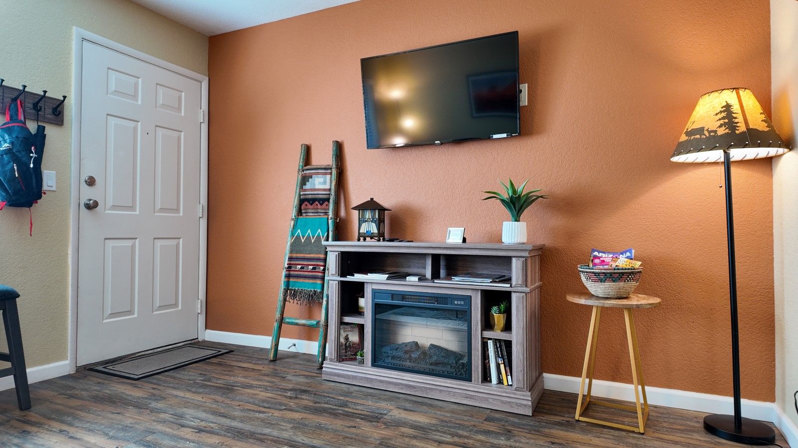 Una sala de estar con chimenea, televisor montado en la pared, una escalera y una lámpara.