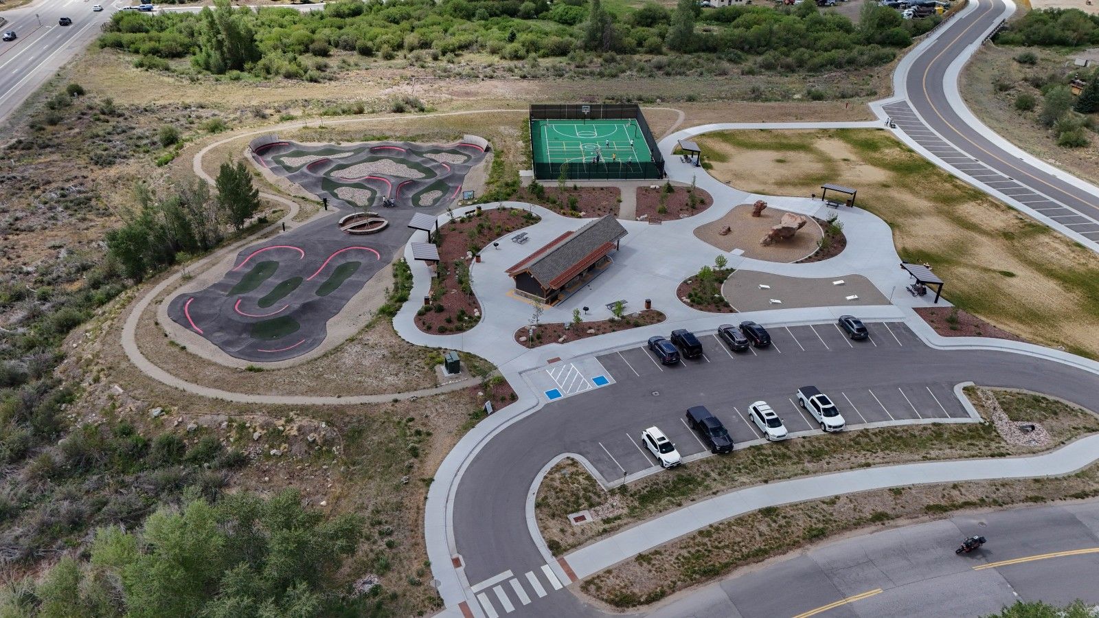 Une vue aérienne d’un parking où sont garées plusieurs voitures, d’un terrain de basketball et d’un bâtiment doté d’un toit végétalisé.
