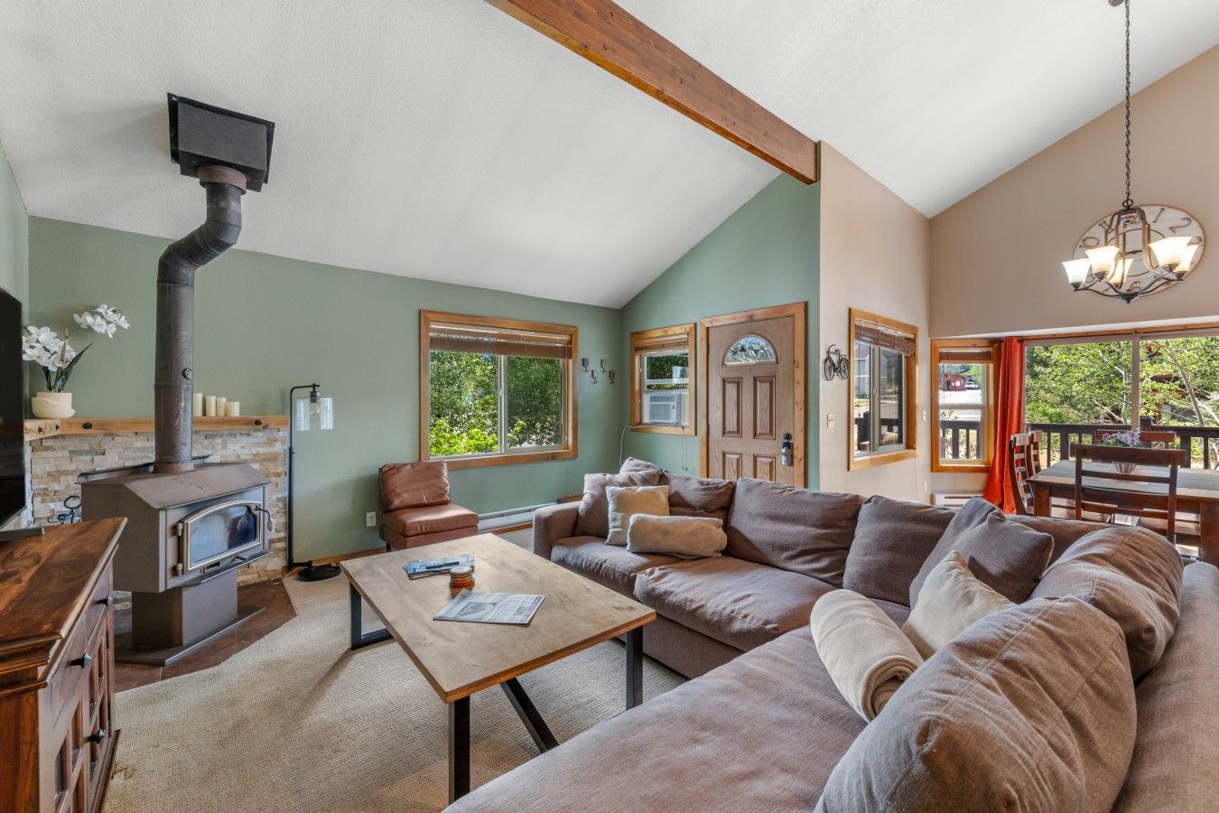 A cozy living room with a fireplace, a sofa, a dining table, and a view of the outdoors.