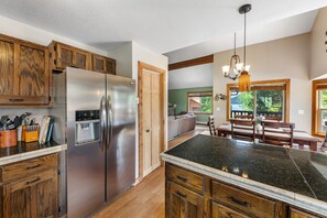 A kitchen with wooden cabinets, a stainless steel refrigerator, a granite countertop, and a dining area with wooden furniture.