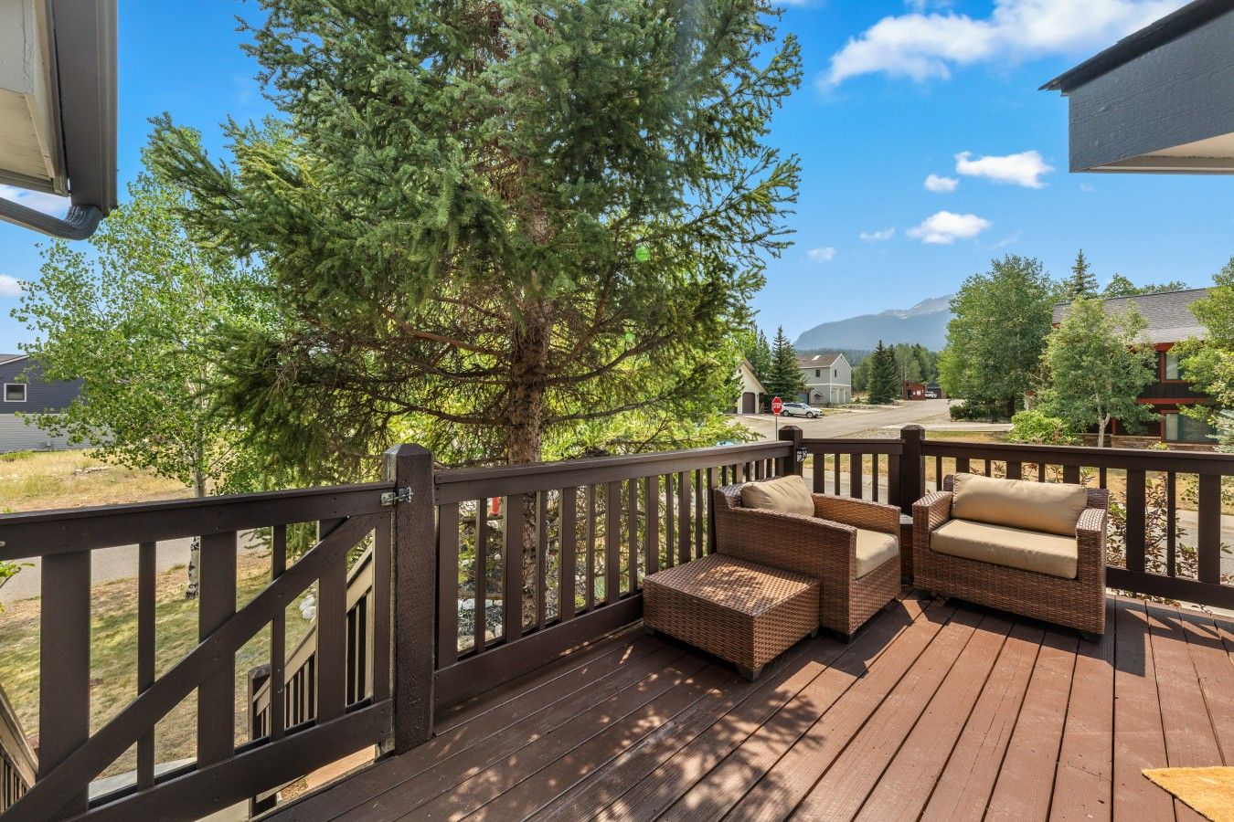 A wooden deck with wicker furniture and a view of a residential area with trees and houses.
