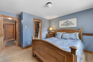 A bedroom with a wooden bed, a nightstand, a wall-mounted lamp, and a framed picture. - Rabbit House | Your Summit County Mountain Retreat (Silverthorne)