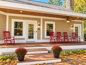 A covered porch with red chairs, a white door, and a stone pillar. - South Main Street Cottage - Leland, Michigan - Saturday to Saturday (Leland)
