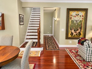 A staircase leading to an upper floor, a dining area with a round table and checkered chairs, and a large framed painting on the wall. - South Main Street Cottage - Leland, Michigan - Saturday to Saturday (Leland)